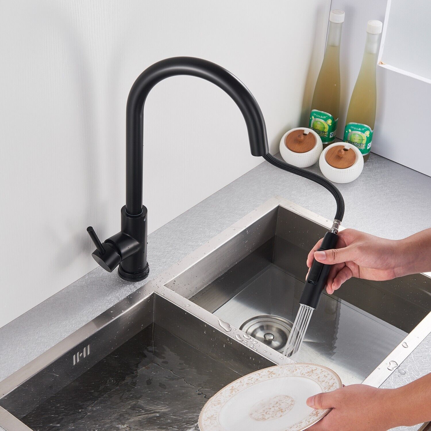 Person using a black kitchen faucet with a handheld spray head over a sink.