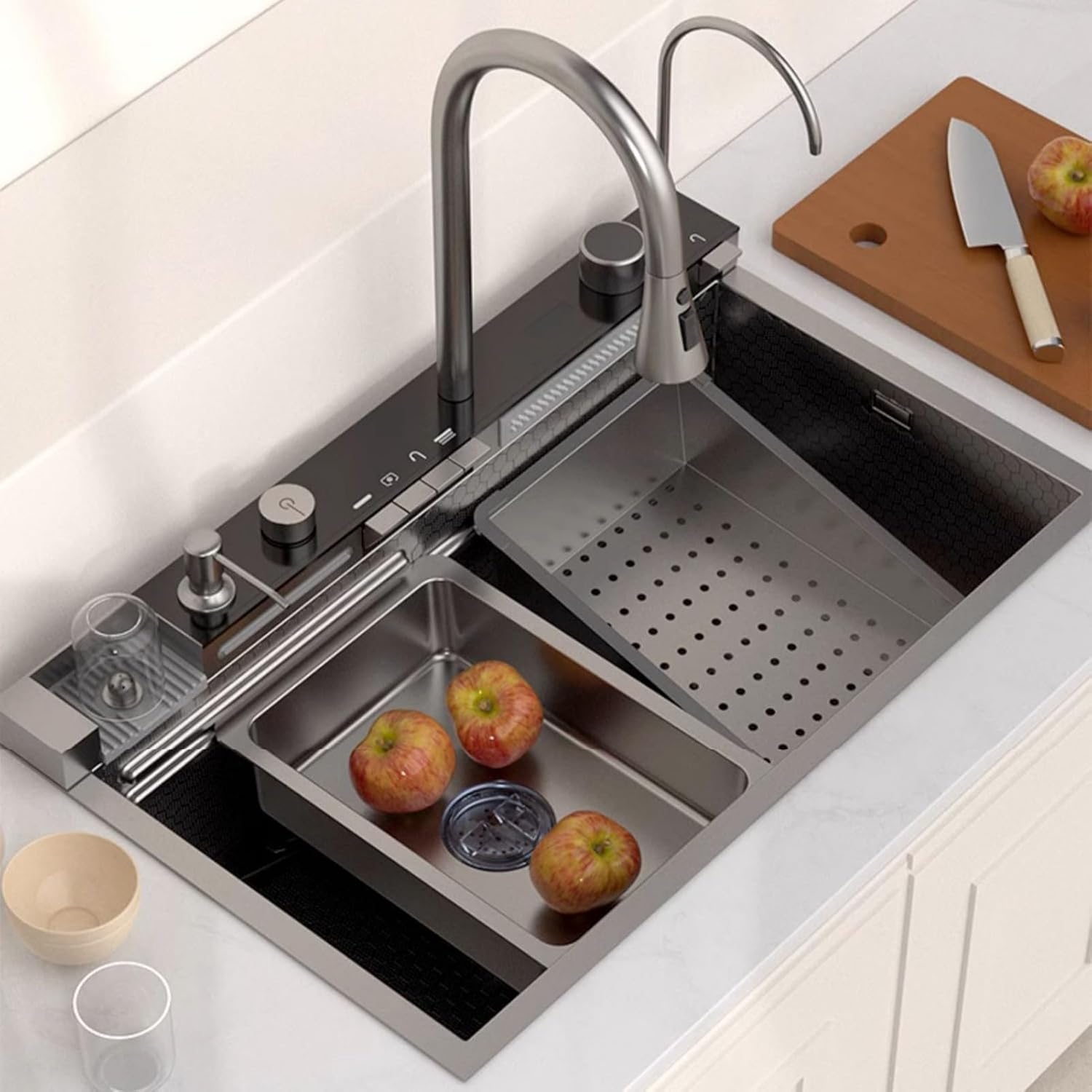 Stainless steel kitchen sink with apples and a cutting board on a white countertop